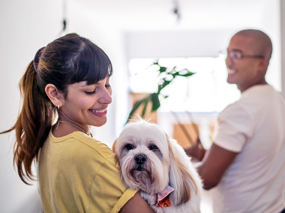 Woman holding her small white dog with partner.