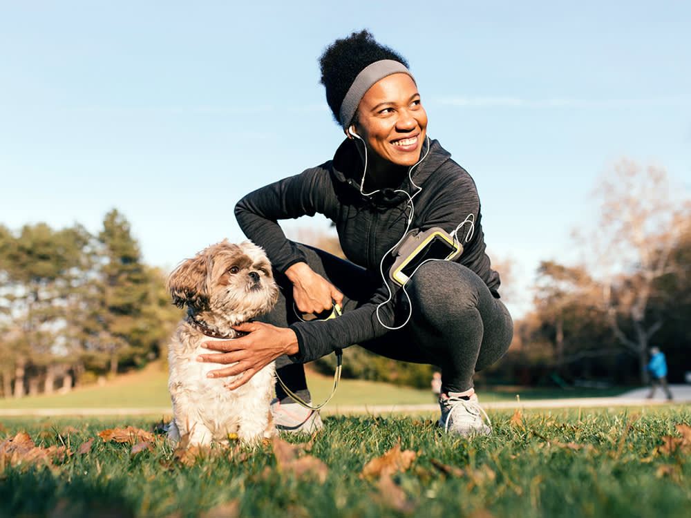 woman in running gear petting a small dog in a park