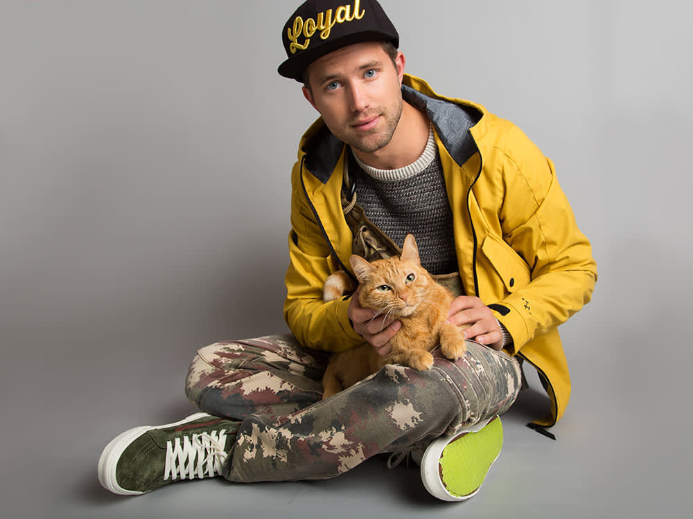 Nathan sitting on the floor with a cat in front of a gray background