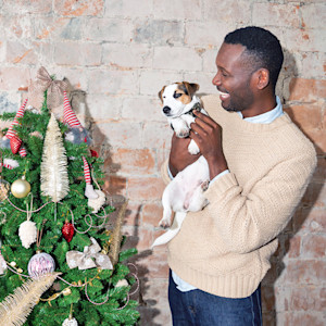 a man hugs a jack russell next to a Christmas tree