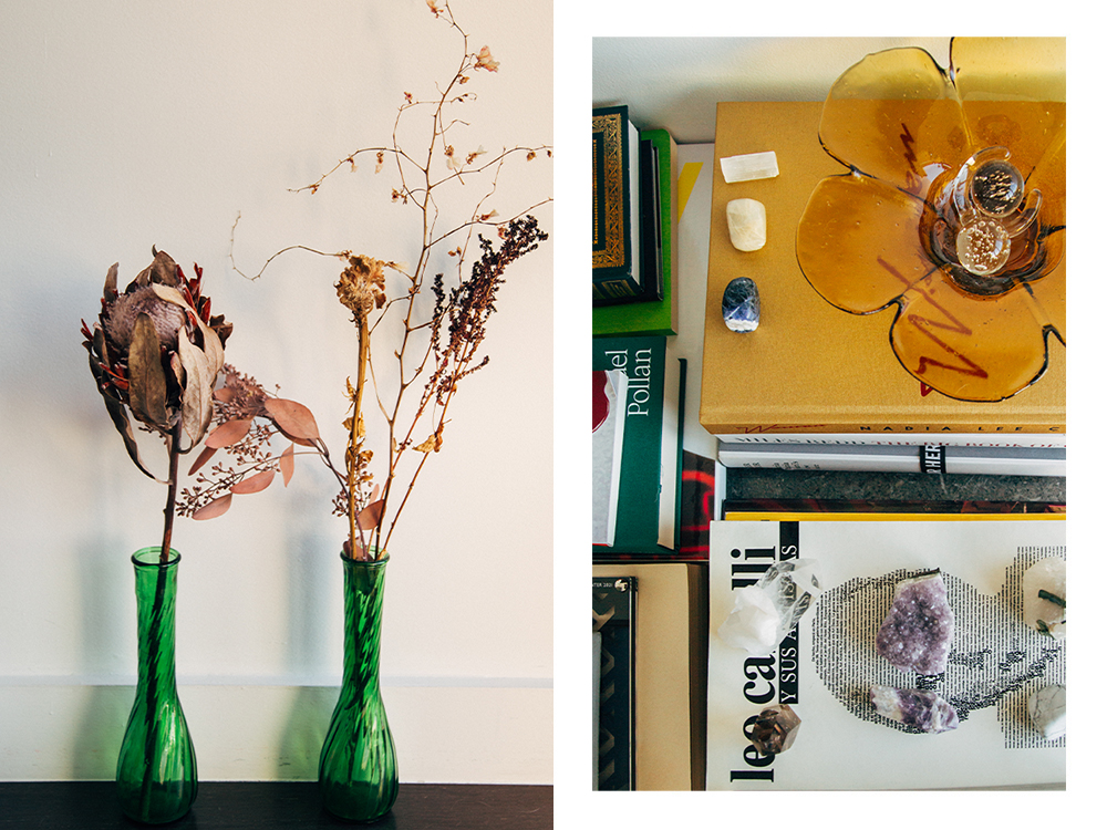 two green vases with dried flowers inside; piled books with crystals and a floral dish on top 