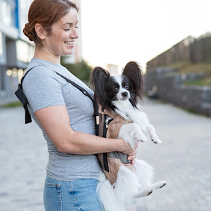 Woman with her small dog in a baby carrier outside.