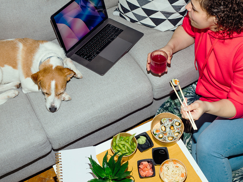 Woman eating sushi while her dog sleeps on the couch.