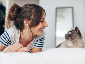 Smiling Woman And Cat Looking Each Other In The Bedroom.
