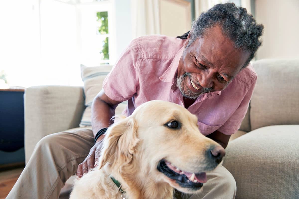 a Black man smiles while he pets his dog