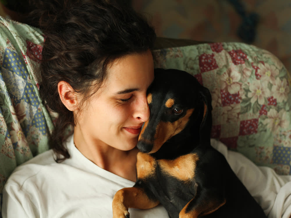 Young woman hugging her small black dog on the couch 