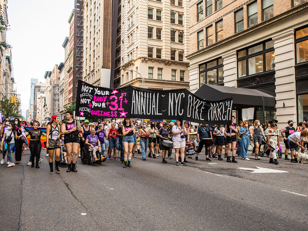 People march with the Dyke March 2023 banner, which reads, Not Your “F*cking Body, Not Your F*cking Business.”