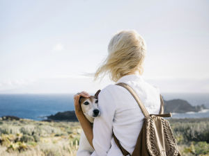 A woman holding a dog in her arms while looking at a scenic view of the sea.