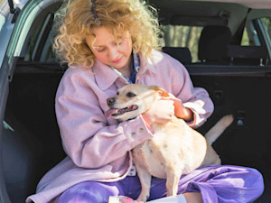 Woman looking intently at her dog's fur while sitting in the trunk of a car.