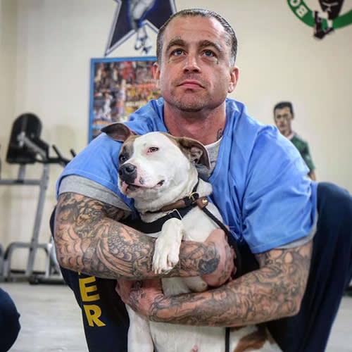 an incarcerated man hugs a white dog 