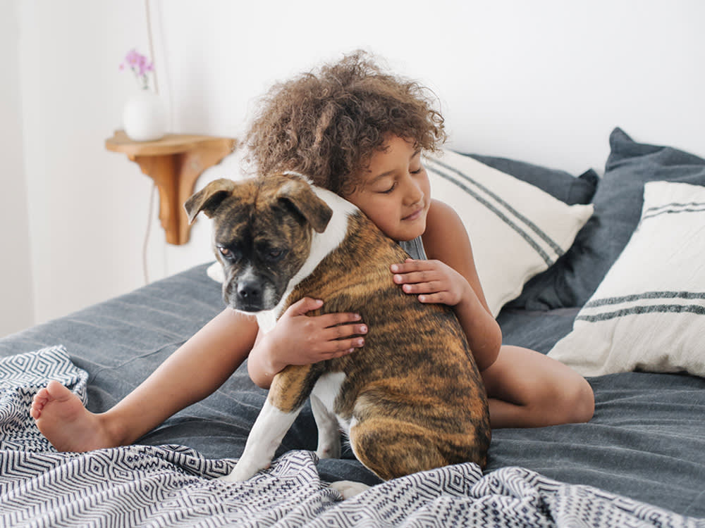 a small child with curly hair hugs a dog on a bed