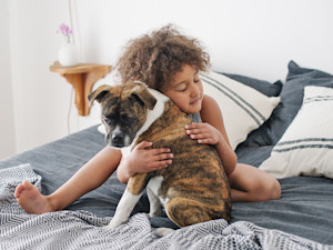a small child with curly hair hugs a dog on a bed