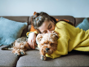 A shot of a young woman hugging lovely her little dog while lying down on the sofa in her living room.