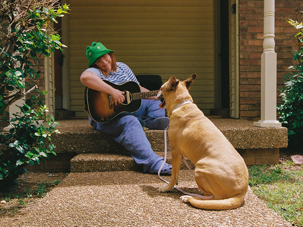 Corook sits on a front porch and plays guitar for Cubby