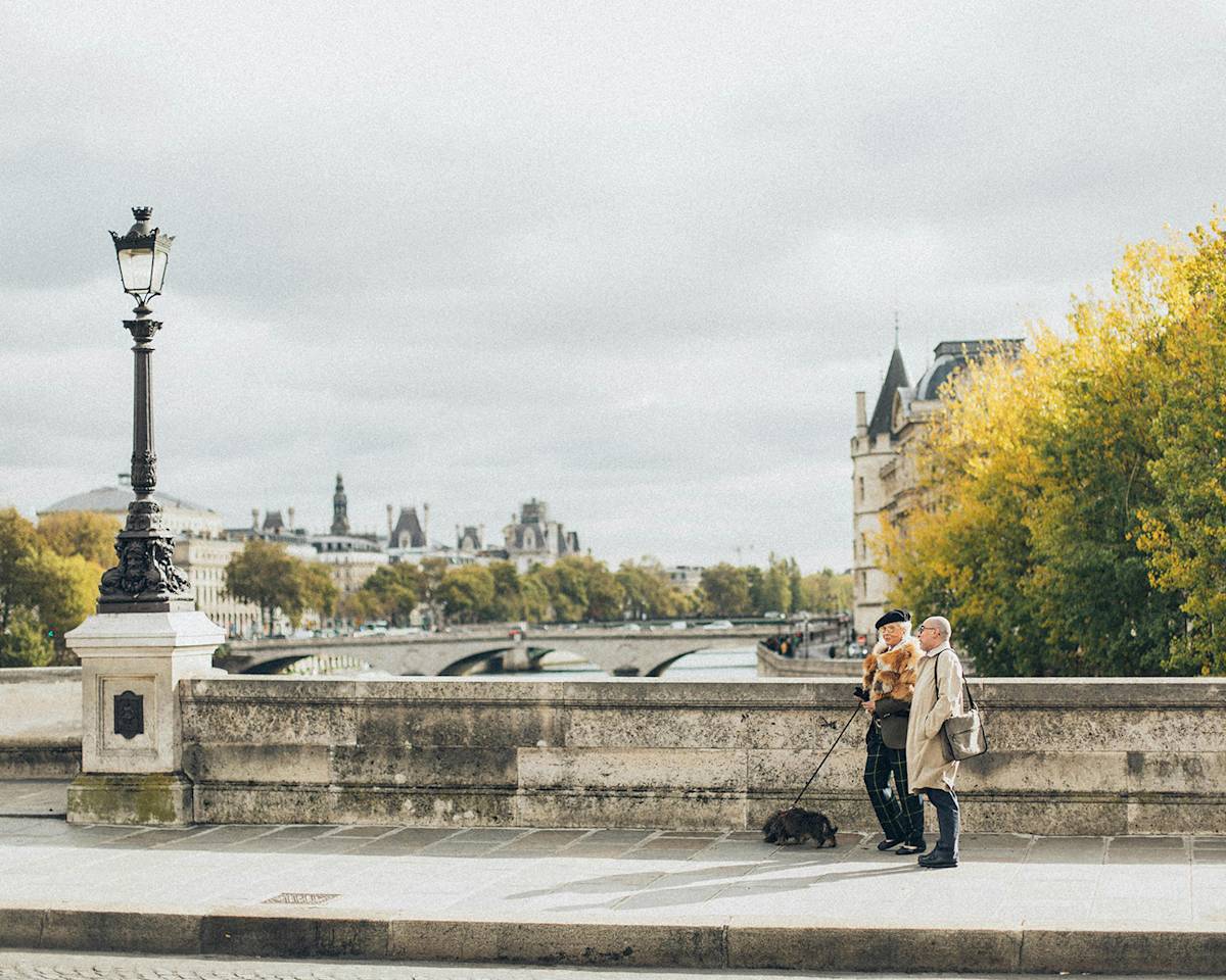 couple walking a dog on a bridge on the seine in Paris, France