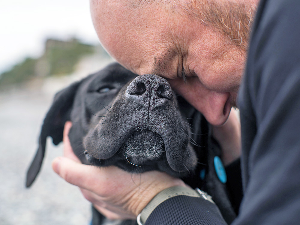 Man snuggling his dog outside.