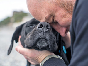 Man snuggling his dog outside.