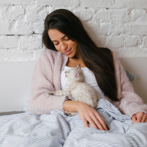Young beautiful woman cuddling with little snow bengal kitten on the bed.