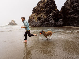 A man running and playing with his German Shepherd dog on a cloudy and rocky beach