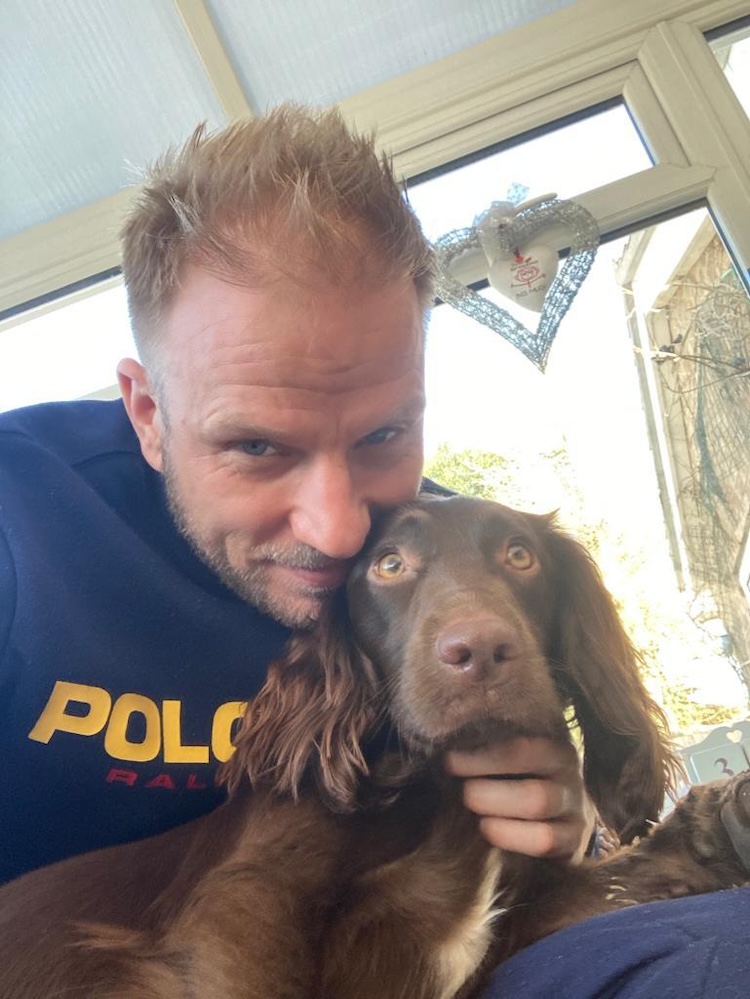a man with blond hair hugs a brown cocker spaniel