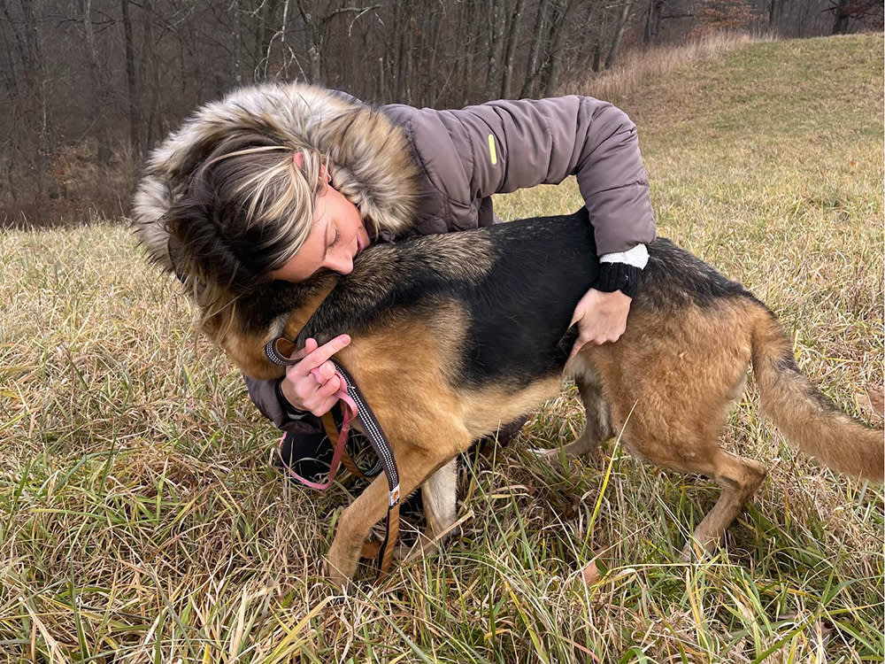 Woman in a coat soothing a rescued German Shepherd dog in a field outside
