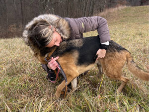 Woman in a coat soothing a rescued German Shepherd dog in a field outside