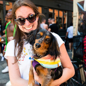 Black and tan dog wearing a rainbow scarf in a woman's arms at The Wildest Pride Parade