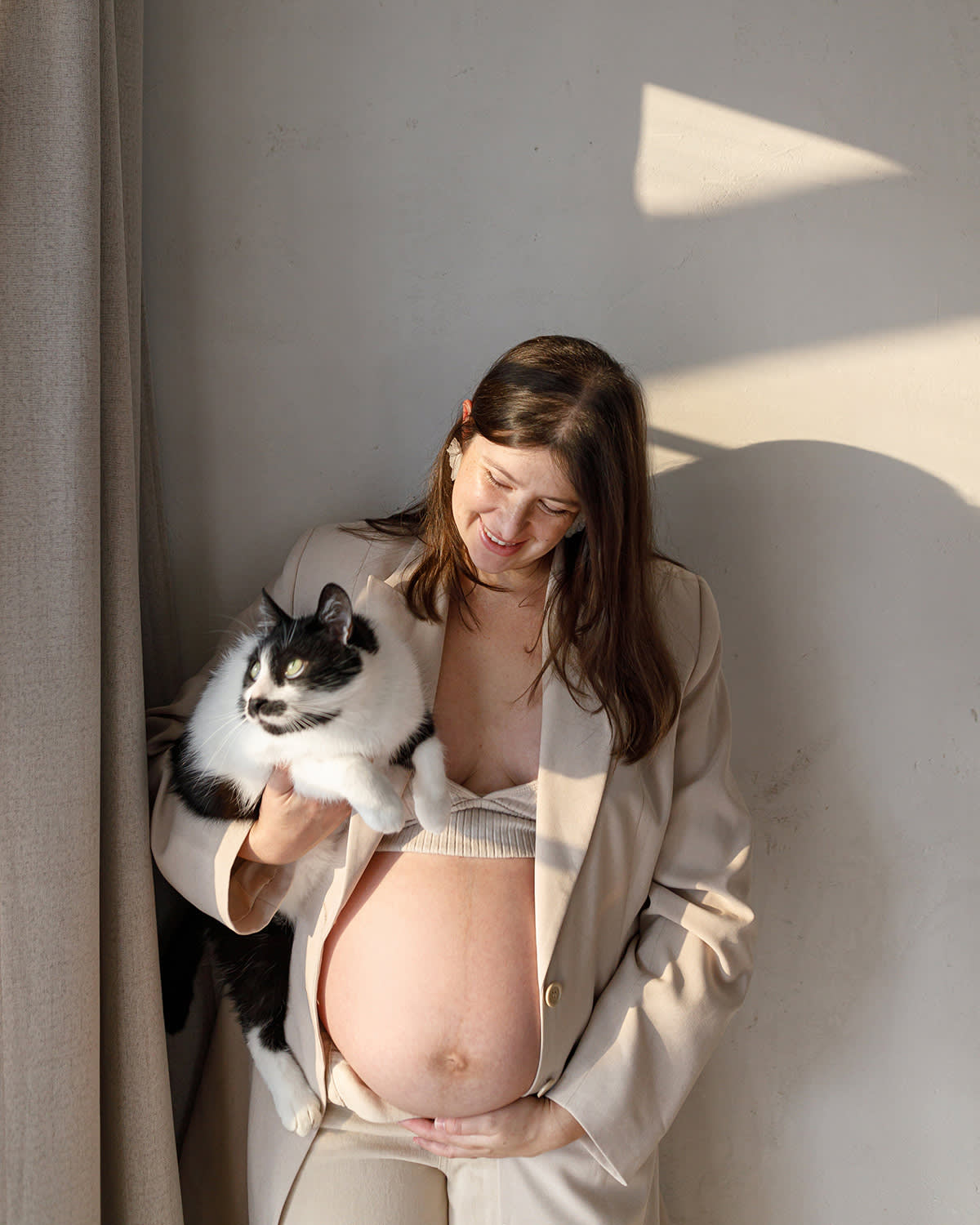 a picture of a pregnant woman wearing a suit and no shirt with her belly out holding a black and white cat