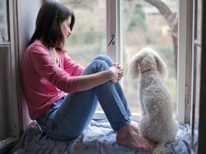 Woman looking out window with small white dog.