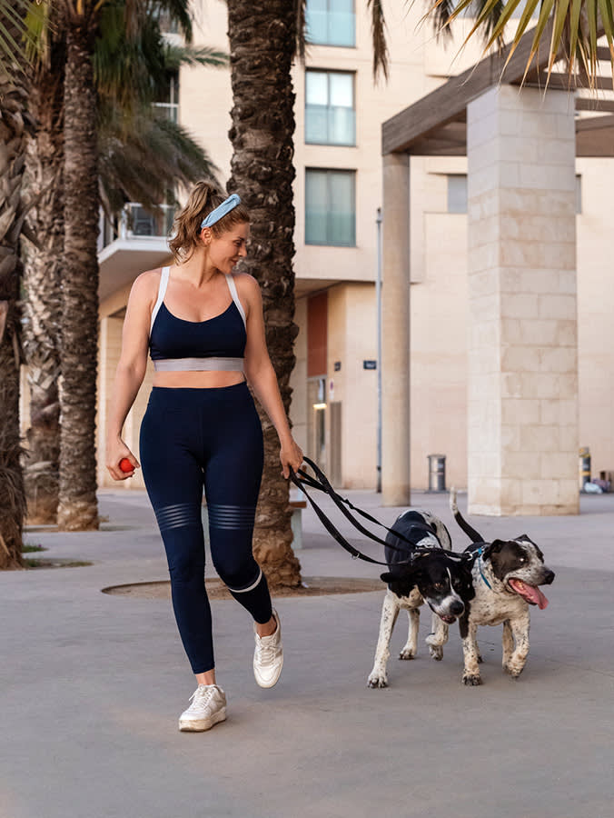 Woman In Sportswear Walking With Two Dogs On The Street.