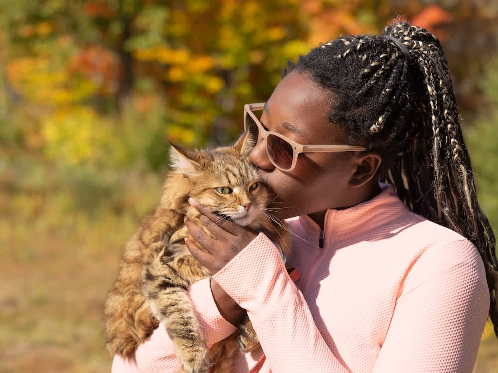 a picture of a woman in a pink top kissing her long haired tabby cat outside