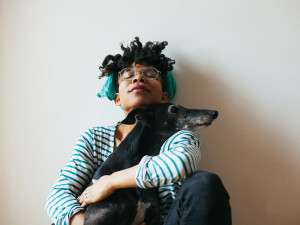 Woman spending time with her with greyhound dog sitting in front of a white wall.