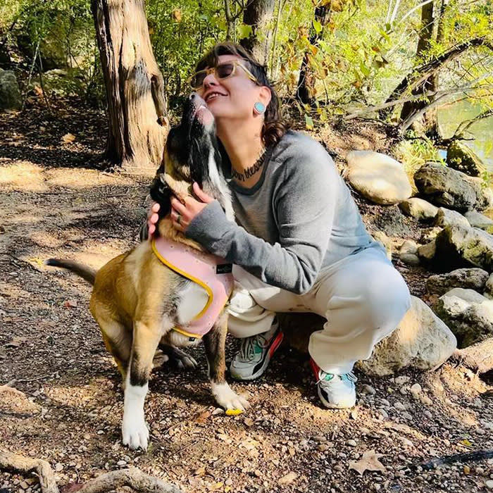person crouching with dog licking their face