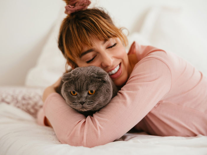 A woman smiling and hugging her cat on a bed. 