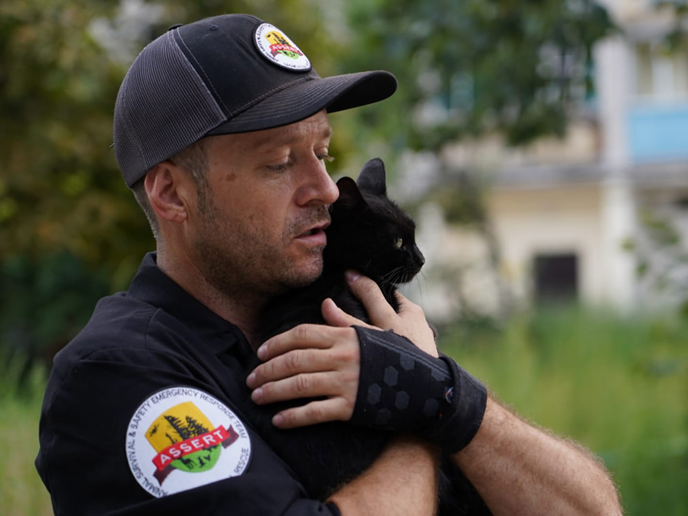 Douglas Thron, in his rescue pilot uniform hugging a rescued black cat to his chest outside