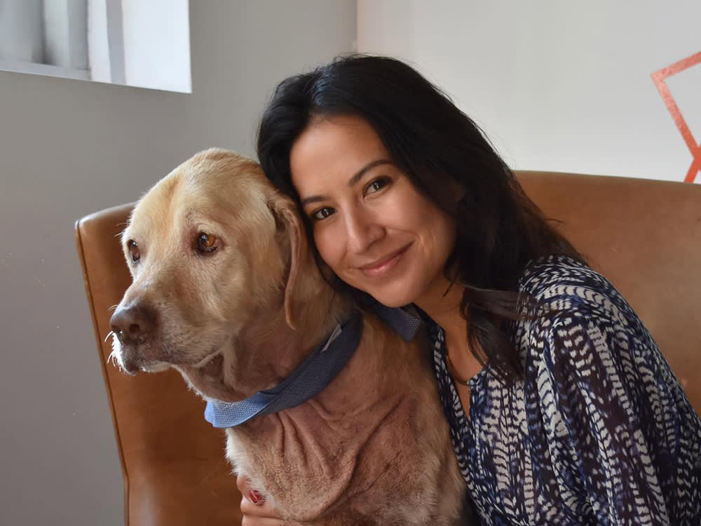 Hope Reiner smiling at the camera seated in a brown chair hugging a Golden Retriever rescue dog named Oliver