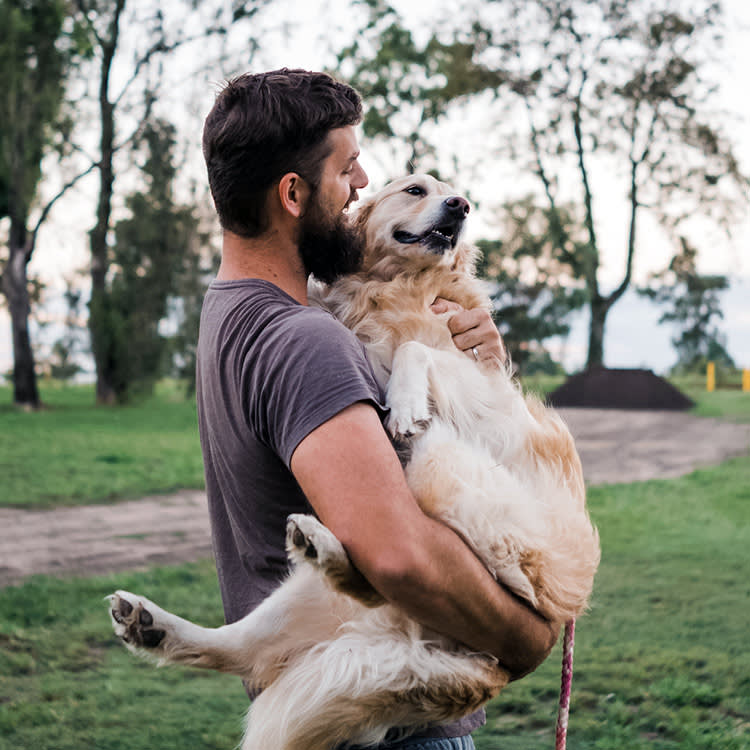 Man holds his Labrador dog in his arms outside.