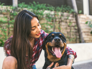 Young woman is hugging her Rottweiler dog while they sit outside on the street.