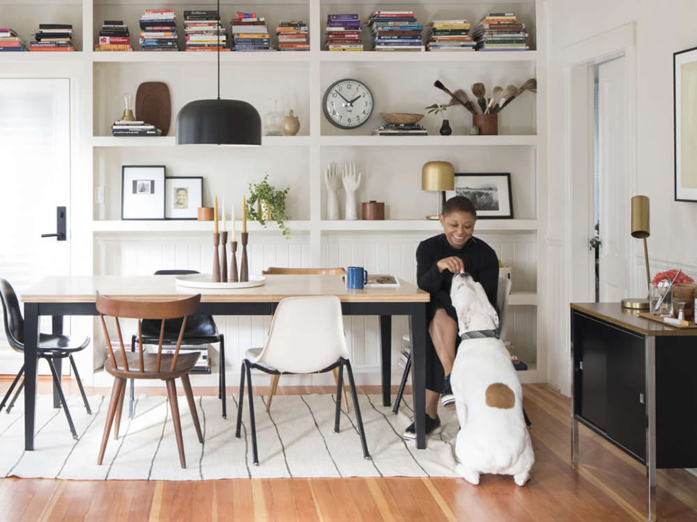 A woman sitting at a dining room table with a dog. 