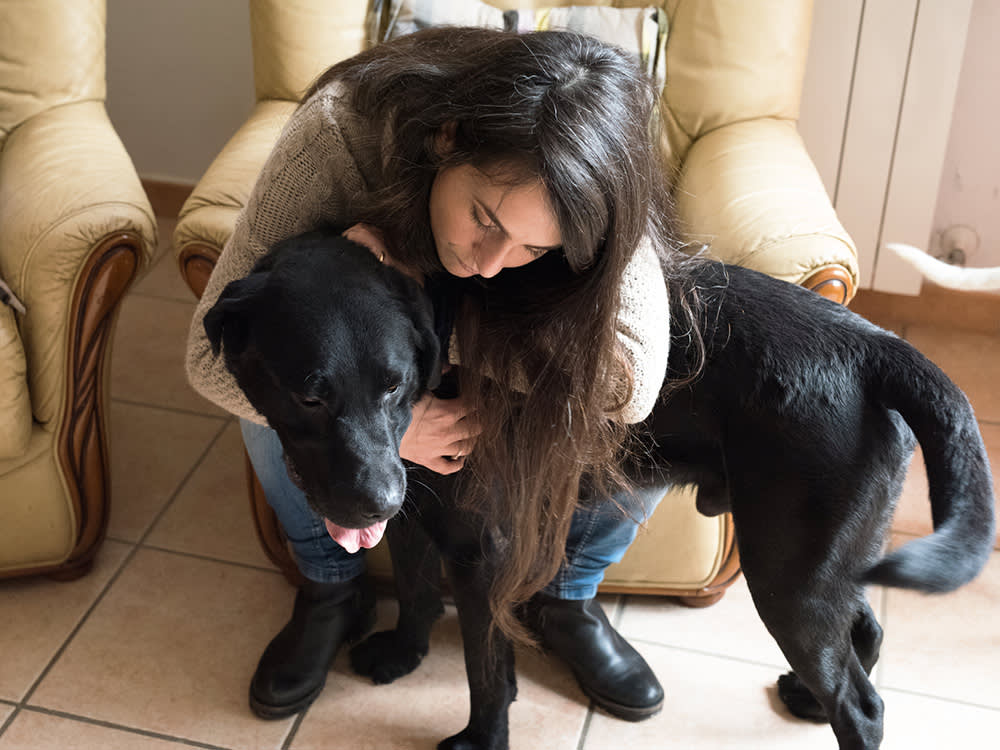 A woman hugging a black lab in her arms. 