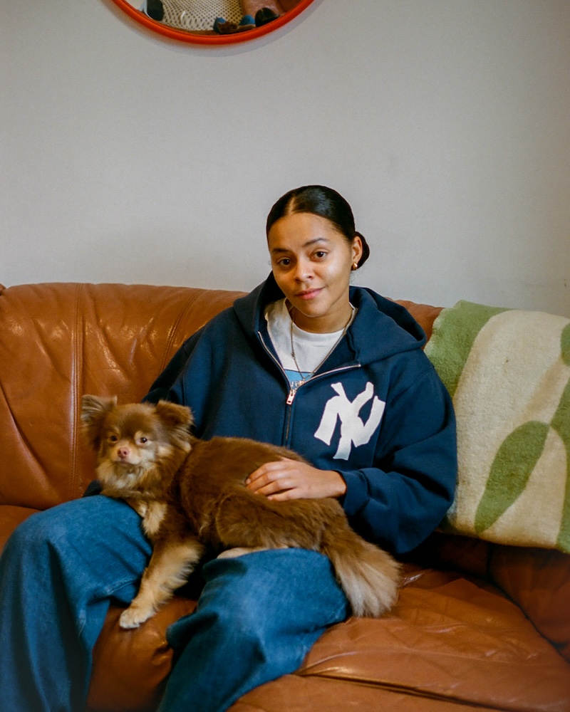 a woman with black hair sits on a leather couch with a brown dog on her lap