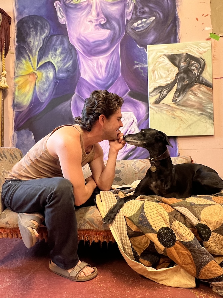 a man and a greyhound pose nose to nose in front of a large painting