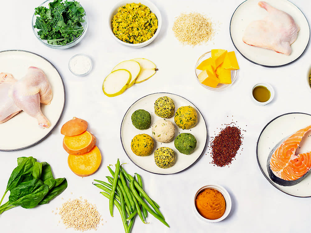 a table covered with Migos pucks and ingredients: raw chicken, fish, asparagus 