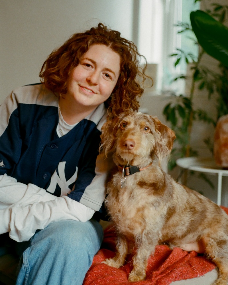 a woman with curly red hair poses with a small dog