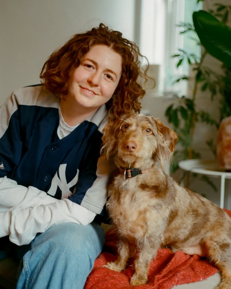 a woman with curly red hair poses with a small dog