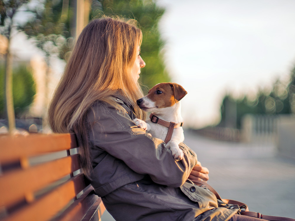 Woman sitting on a bench with her dog in her lap.