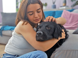 Woman cuddling her sick black dog at home.