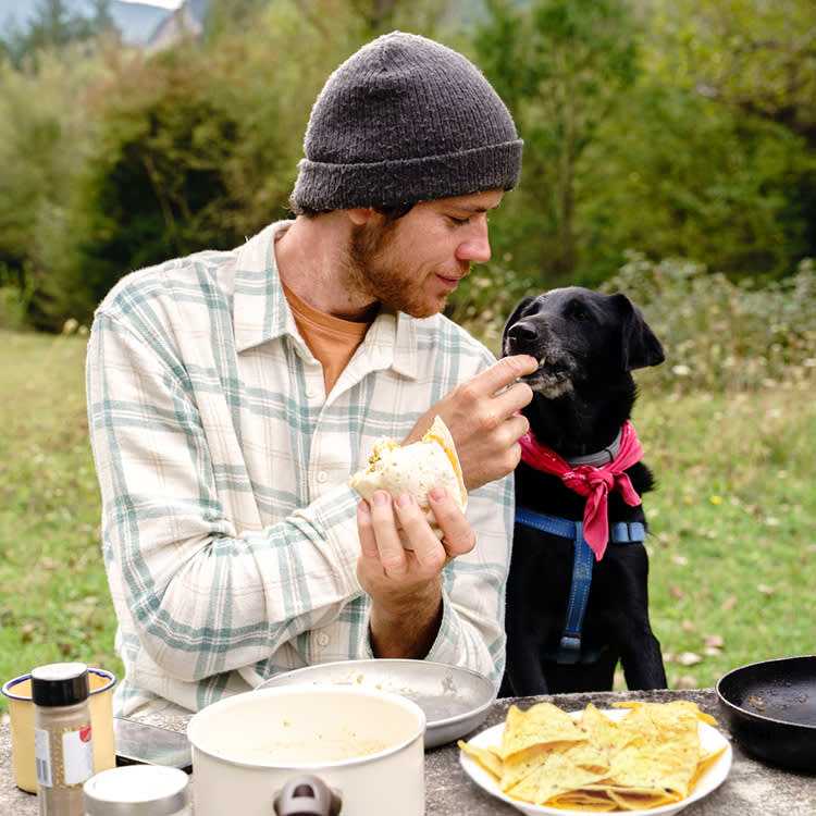 Man eating tortilla chips outside with his dog.