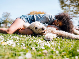 A Young Woman Rests in the Grass With Pet Poodle Dog.