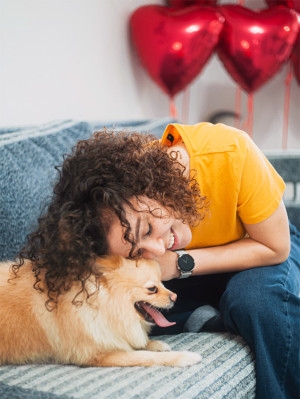woman with curly brown hair cuddles up to her dog with red heart balloons